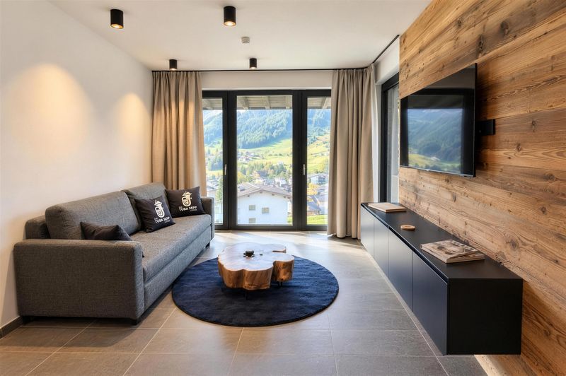 Wohnzimmer mit grauem Sofa, Baumstamm-Tisch, Altholzwand und Fernseher