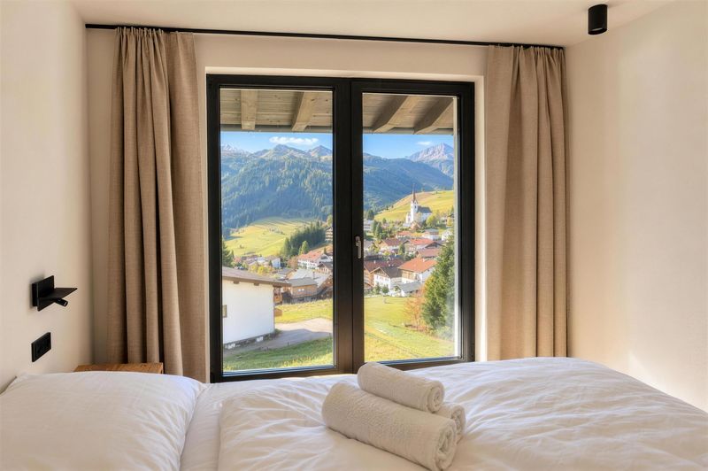 Blick vom Bett durch die Balkontür auf das Dorf und die Berge
