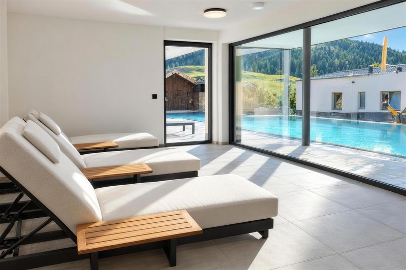 Ruheraum mit weißen Liegen und Glasfront zum Pool